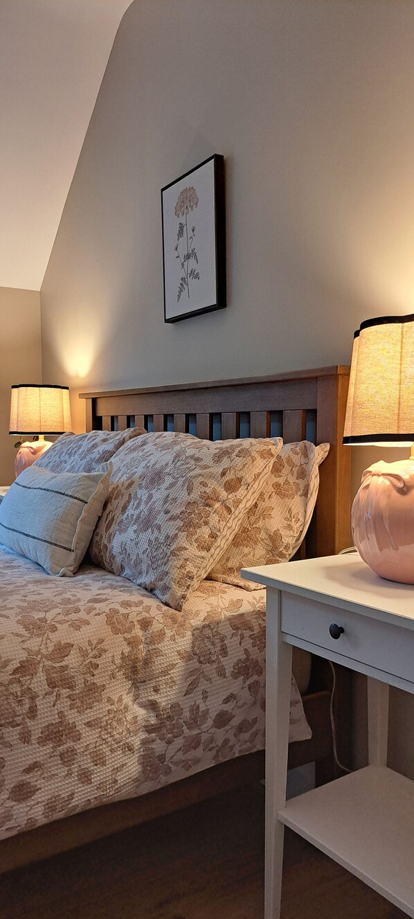 A bedroom with a bed, two bedside lamps, a framed picture on the wall, and a nightstand with a lamp.