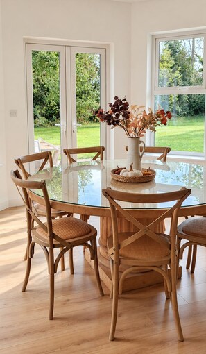 A dining area with a glass table surrounded by wooden chairs, a vase with dried flowers, and a basket with pumpkins.