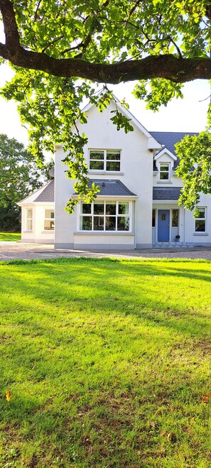 A two-story house with a large front lawn, a garage, and a driveway.