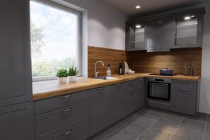 A modern kitchen with grey cabinets, a wooden countertop, a built-in oven, and a window with a view of greenery. - Holiday home with 6 bedrooms (Blekendorf OT Sehlendorf)