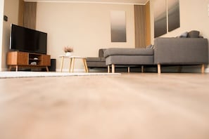 Ein modernes Wohnzimmer mit einem grauen Sofa, einem Holz-TV-Schrank und einem kleinen weißen Tisch.