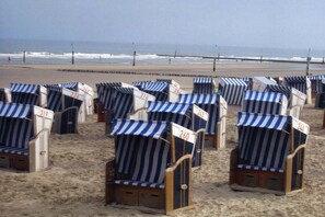 Rows of beach chairs with numbers on them, arranged on a sandy beach with the ocean in the background. - Apartment 17, Südstrasse 1 (Norderney)