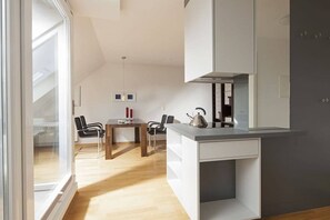 A modern kitchen with a dining area, a kettle, and a window providing natural light. - Apartment 17, Südstrasse 1 (Norderney)