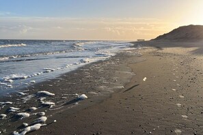 Ein Strand mit Wellen, ein weiter Pier im Hintergrund und ein Hügel.