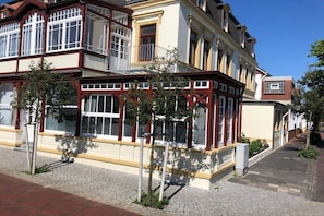 Ein mehrstöckiges Gebäude mit großen Fenstern und einem Balkon, an einer gepflasterten Straße gelegen.