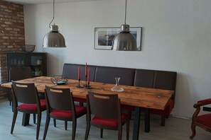 A dining area with a wooden table, red cushioned chairs, a bench, and pendant lights. - Holiday home in Remagen with barbecue (Remagen)