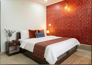 Un dormitorio con cama, mesitas de noche, lámpara de pared y un papel tapiz estampado.