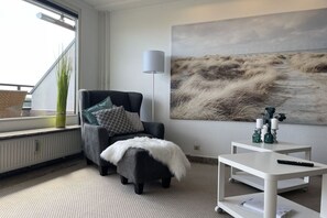 A modern living room with a black armchair, a white side table, and a large abstract painting on the wall. - Penthouse First Line (Damp)