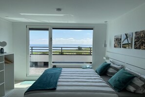 Ein Schlafzimmer mit einem großen Fenster, einem Bett mit gestreifter Bettwäsche und Meerblick.