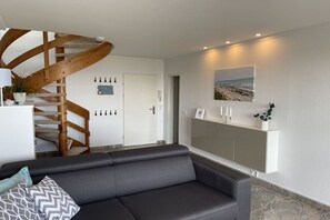 Ein modernes Wohnzimmer mit einem dunklen Sofa, einer Holzspirale, einem weißen Konsolentisch mit einem Bild und einem Marmorboden.