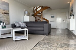 A modern living room with a grey sofa, a white coffee table, and a spiral staircase. - Penthouse First Line (Damp)
