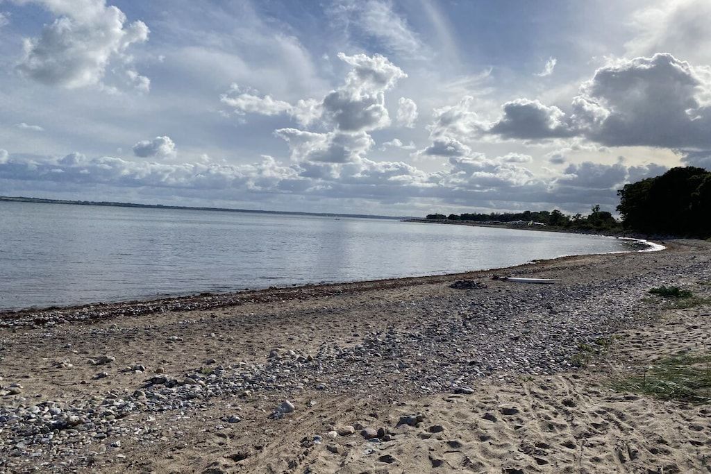 A beach with pebbles and sand, a calm sea, and a partly cloudy sky.