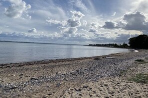 Ein Strand mit Kieselsteinen und Sand, ein ruhiges Meer und ein teilweise bewölkter Himmel.