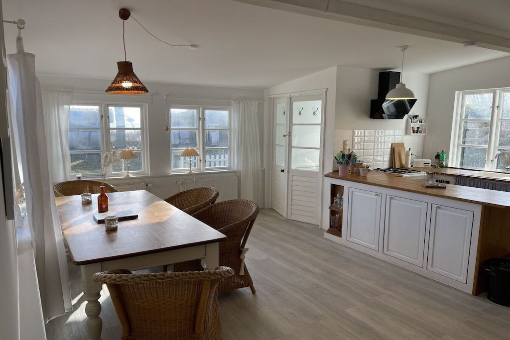 A kitchen with a dining table, wicker chairs, pendant lighting, and white cabinetry.