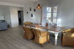 Ein Essbereich mit einem Holztisch, Korbstühlen, einer Pendelleuchte und einem Fenster mit Vorhängen.