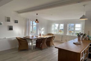 Ein geräumiges Zimmer mit Esstisch, Korbstühlen, einer Holztresen und großen Fenstern.