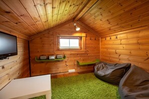 A cozy cabin interior with a television, a window, a green carpet, and bean bags. - Archipelago house type D (Neustadt\/Holstein - OT Pelzerhaken)