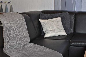 Ein schwarzes Ledersofa mit einer grauen, gemusterten Decke und zwei Kissen, eines mit einem Rundmuster und das andere mit einem flauschigen Rand.