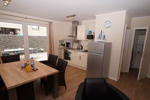 A compact kitchen with a refrigerator, microwave, and oven. There is a dining area with a table and chairs, and a view of the outside through a glass door. - HUS PIA Apt. 1 "Helgoland" (Cuxhaven)