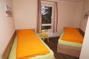 A small room with two single beds, a window with curtains, a radiator, and a chair. - HUS PIA Apt. 3 "Scharhörn" (Cuxhaven)