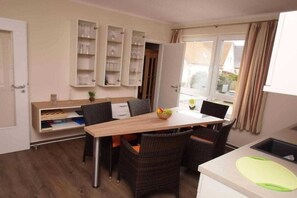 Eine kompakte Küche mit Essbereich, ausgestattet mit einem eingebauten Schrank für Gläser, einem kleinen Tisch mit Stühlen und einem Fenster mit Vorhängen.