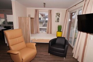 A living room with a sofa, a chair, a flat-screen TV, and a window with curtains. - HUS PIA Apt. 3 "Scharhörn" (Cuxhaven)