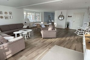 A spacious living area with a sofa, armchairs, a coffee table, and a dining table. - Holiday home with 1 bedroom (Timmendorfer Strand)