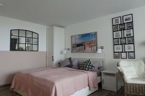 Ein Schlafzimmer mit einem Bett, Nachttischen, einem Sessel, einem Spiegel und einer Wand mit gerahmten Bildern.