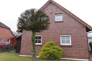 Ein Ziegelhaus mit zwei Fenstern, ein Baum davor und ein rotes Auto in der Nähe geparkt.