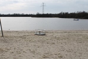 Ein sandiger Strand mit einer Metallkonstruktion, einem Gewässer und einem weit entfernten Strommasten.