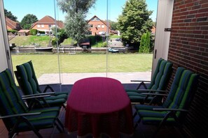 Eine Terrasse mit Tisch und Stühlen, eine Glastür, die zu einem Hinterhof mit Rasenfläche, einem kleinen Pool und Häusern im Hintergrund führt.