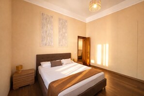 Ein Hotelzimmer mit einem großen Bett, einem Nachttisch, einer Lampe und einer Tür zu einem weiteren Raum.