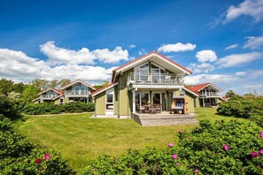 A two-story house with a balcony, surrounded by a well-maintained lawn and flowering bushes. - Captain's House Type F (Neustadt\/Holstein - OT Pelzerhaken)