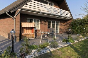 A brick house with a covered patio, outdoor seating, and a small garden. - Holiday home with 3 bedrooms (Dornumersiel-Westeraccumersiel)