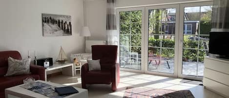 Een moderne woonkamer met een bank, fauteuil, salontafel en een groot raam met uitzicht op de omgeving.