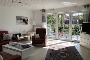 Uma sala de estar moderna com sofá, poltrona, mesa de centro e uma grande janela com vista para o exterior.