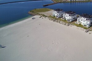 A beachfront property with multiple white buildings, a sandy beach, and a calm body of water. - Holiday home with 4 bedrooms (Kappeln \/ Ostseeresort Olpenitz)