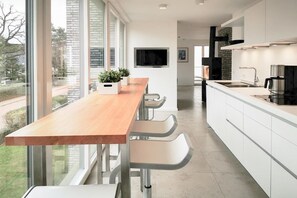 Eine moderne Küche mit einer Holzarbeitsplatte, weißen Schränken und einem großen Fenster mit Blick ins Freie.