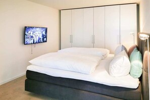 Ein Schlafzimmer mit einem Bett, einem an der Wand montierten Fernseher und einem Kleiderschrank mit Schiebetüren.