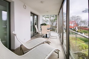 Ein Balkon mit zwei weißen Korbsesseln, einem kleinen Tisch mit einer Pflanze und Blick auf eine Wohngegend.