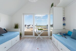 Ein modernes Schlafzimmer mit Balkon, weißen Möbeln und Meerblick.