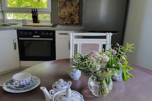 A kitchen with a stove, oven, and a dining table set with a teapot, cups, and a vase of flowers. - Holiday apartment with 2 bedrooms (Hameln)