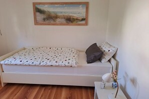 A single bed with a patterned bedspread, a gray pillow, and a small bedside table with a lamp and a vase of flowers. - Holiday apartment with 2 bedrooms (Hameln)
