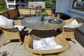 A round outdoor table with wicker chairs, a vase with flowers, and a glass of wine on a balcony. - Holiday apartment with 2 bedrooms (Hameln)