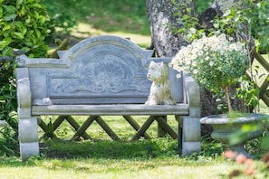 Un banc de pedra amb una escultura de cap de lleó i una jardiniera de pedra amb flors blanques.