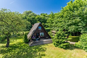 A small, triangular-roofed cabin with a porch, surrounded by lush greenery. - Wangels (Swedish House) (Wangels)