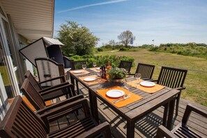 Ein Essbereich im Freien mit Holztisch und -stühlen, einem Grill und Blick auf die umliegende Landschaft.