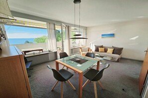 Ein modernes Wohnzimmer mit einem Glastisch, schwarzen Stühlen, einer Couch und Meerblick.