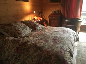 A bed with floral bedding, a bedside lamp, and a wooden headboard in a room with wooden walls. - Right in the Heart of Megève: Comfortable Apartment (Megève)