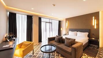A hotel room with a bed, a sofa, a coffee table, and a desk with a lamp.